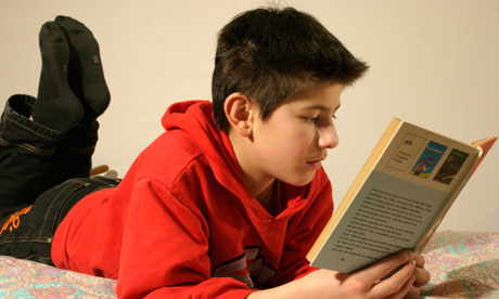 A young boy lying on his bed, reading a book